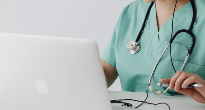 Auf dem Foto sitzt eine junge Frau am Laptop. Sie arbeitet als Medizinische Fachangestellte.