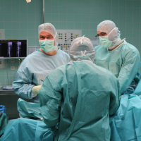 Drei Operateure stehen während einer OP am Operationstisch. Ein Operateur lächelt in die Kamera.
