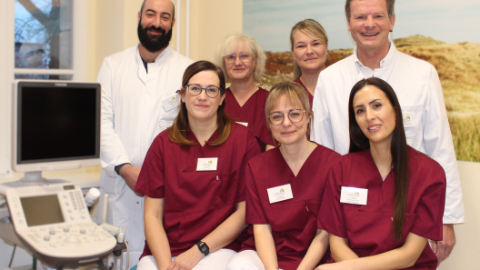 Das Team des Brustzentrums, vier Damen in weinroten Kasaks und links und rechts zwei Herren in weißen Arztkitteln lächeln in die Kamera.